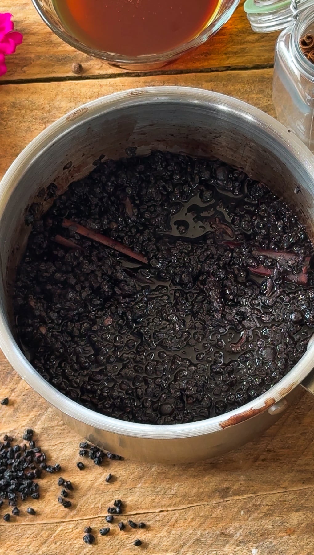 Elderberries simmering in pot on wood surface.