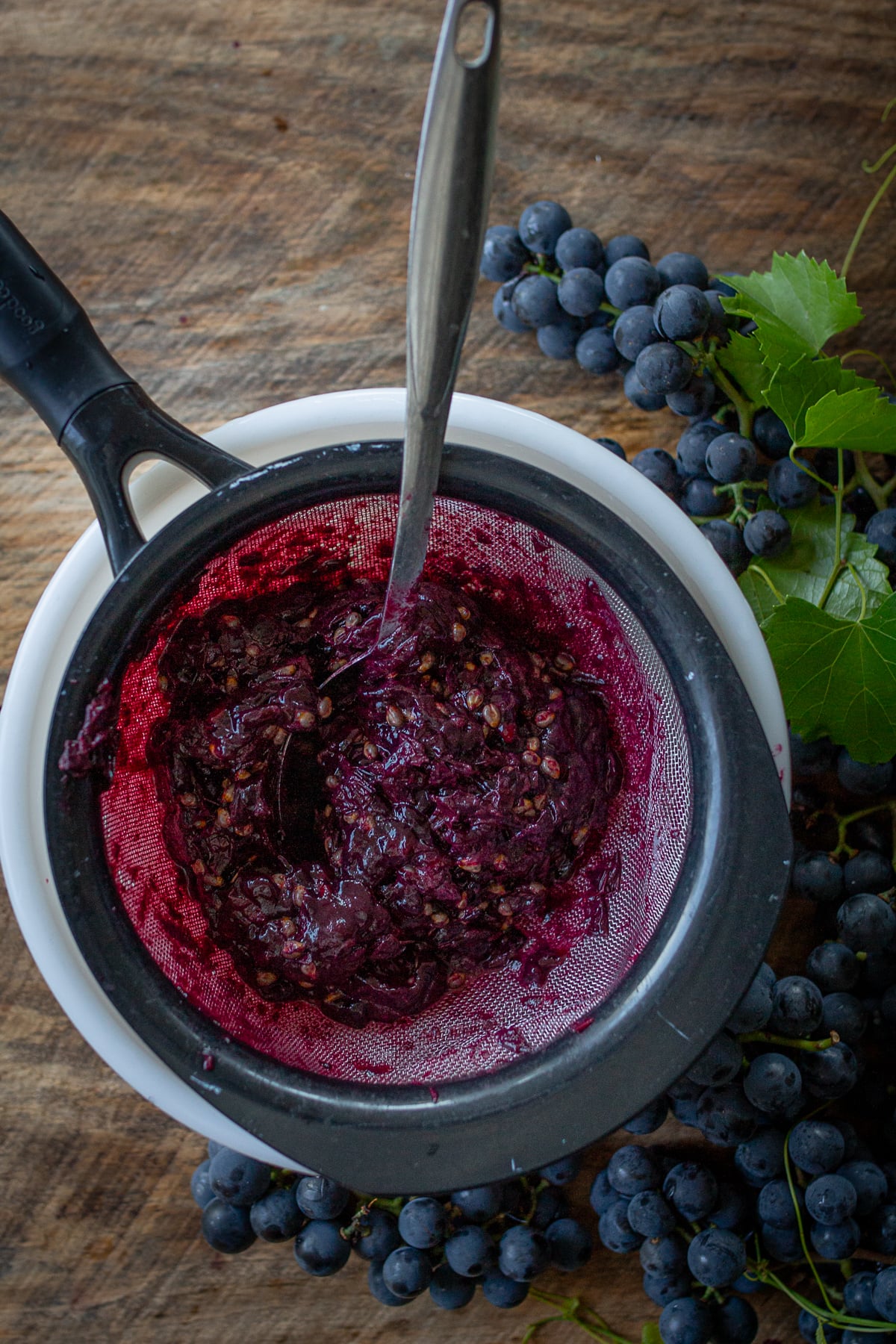 Cooked Concord grapes being pressed through a fine mesh strainer to extract fresh grape juice