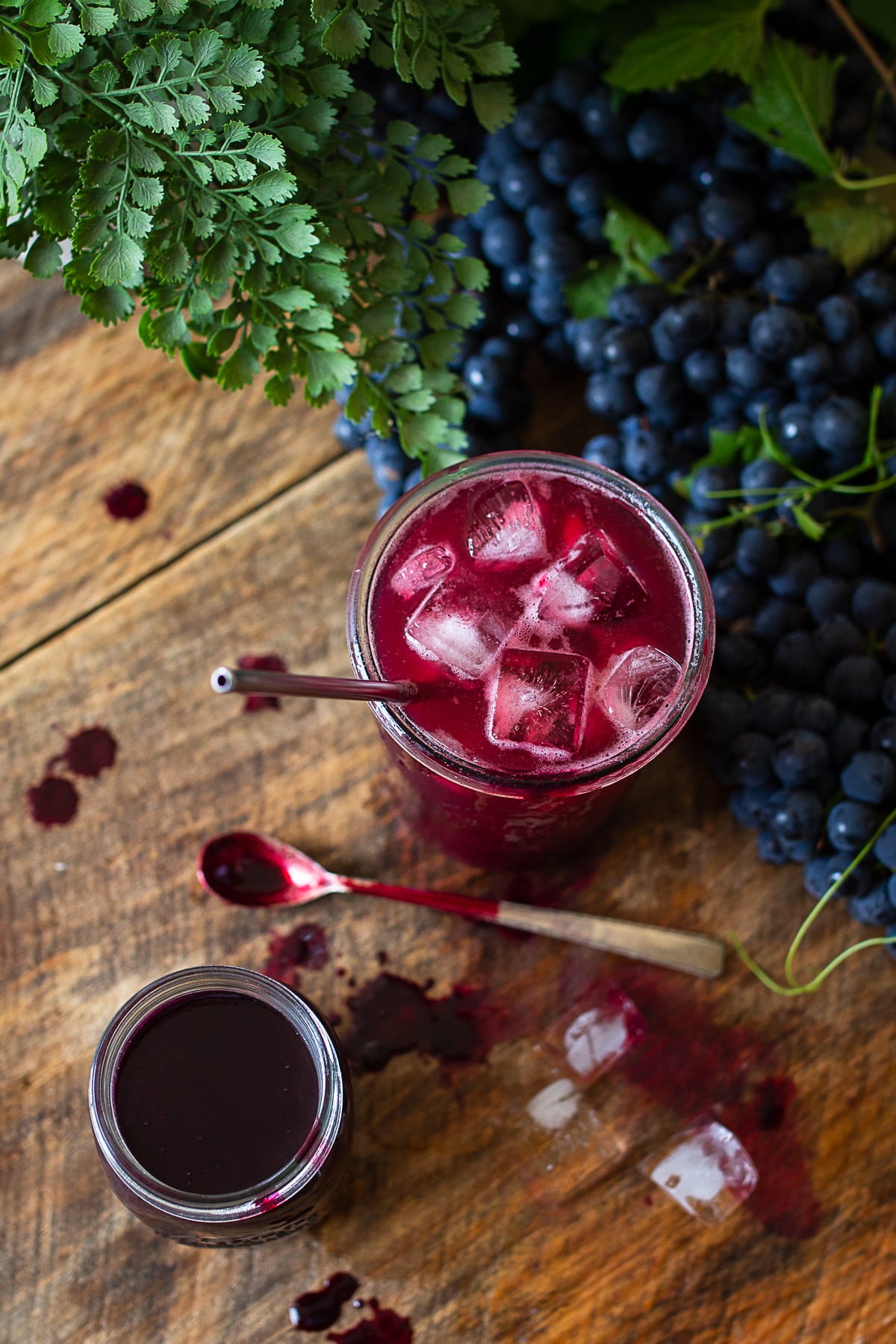 Homemade grape juice concentrate beside a glass of Concord grape juice with fresh grapes