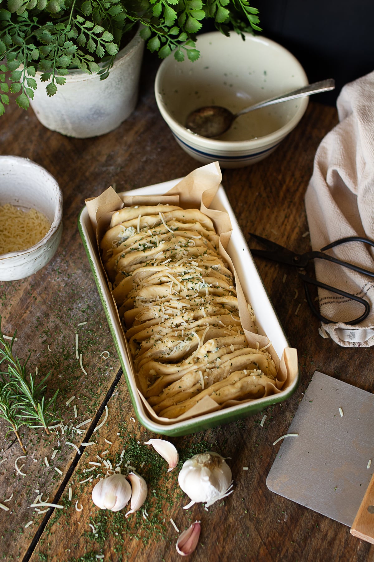 Homemade rosemary garlic pull-apart bread dough being filled with herb butter and parmesan cheese on a rustic farmhouse table.