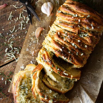 Warm rosemary garlic pull-apart bread with fluffy, buttery layers separating to reveal a soft interior filled with herbs and cheese.