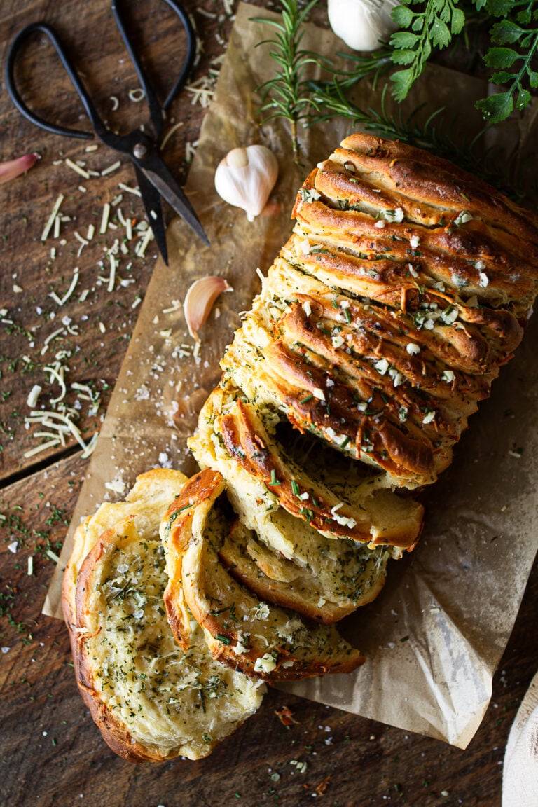 Warm rosemary garlic pull-apart bread with fluffy, buttery layers separating to reveal a soft interior filled with herbs and cheese.