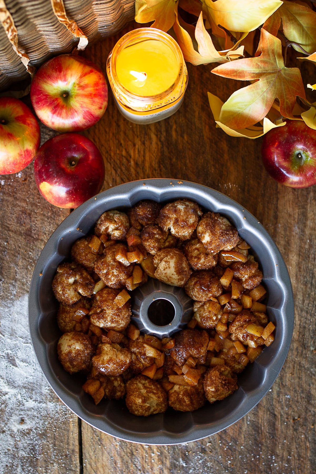 Cinnamon-sugar coated yeast dough balls and diced apples arranged in a grey metal Bundt pan before baking.