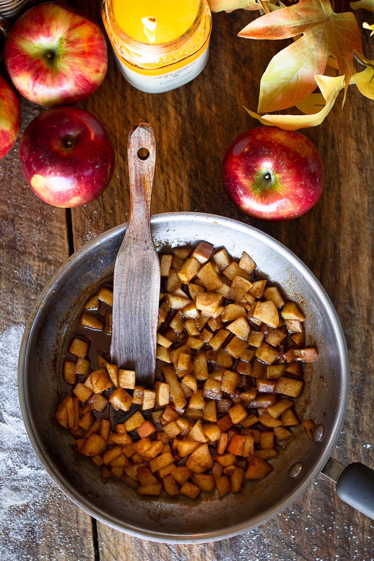 Finely diced apples sauteed in butter and cinnamon sitting in a stainless steel skillet with a wooden spatula.